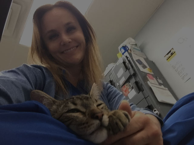 girl smiling towards camera holding a cat on her lap